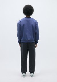 Sudadera azul oscuro con un corte relajado y puños acanalados, combinada con pantalones negros holgados. Se llevan zapatillas con detalles en blanco y negro.