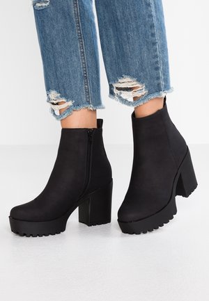 Sorte platform-støvler til anklen med chunky hæle, båret med slidte, blå cropped jeans.