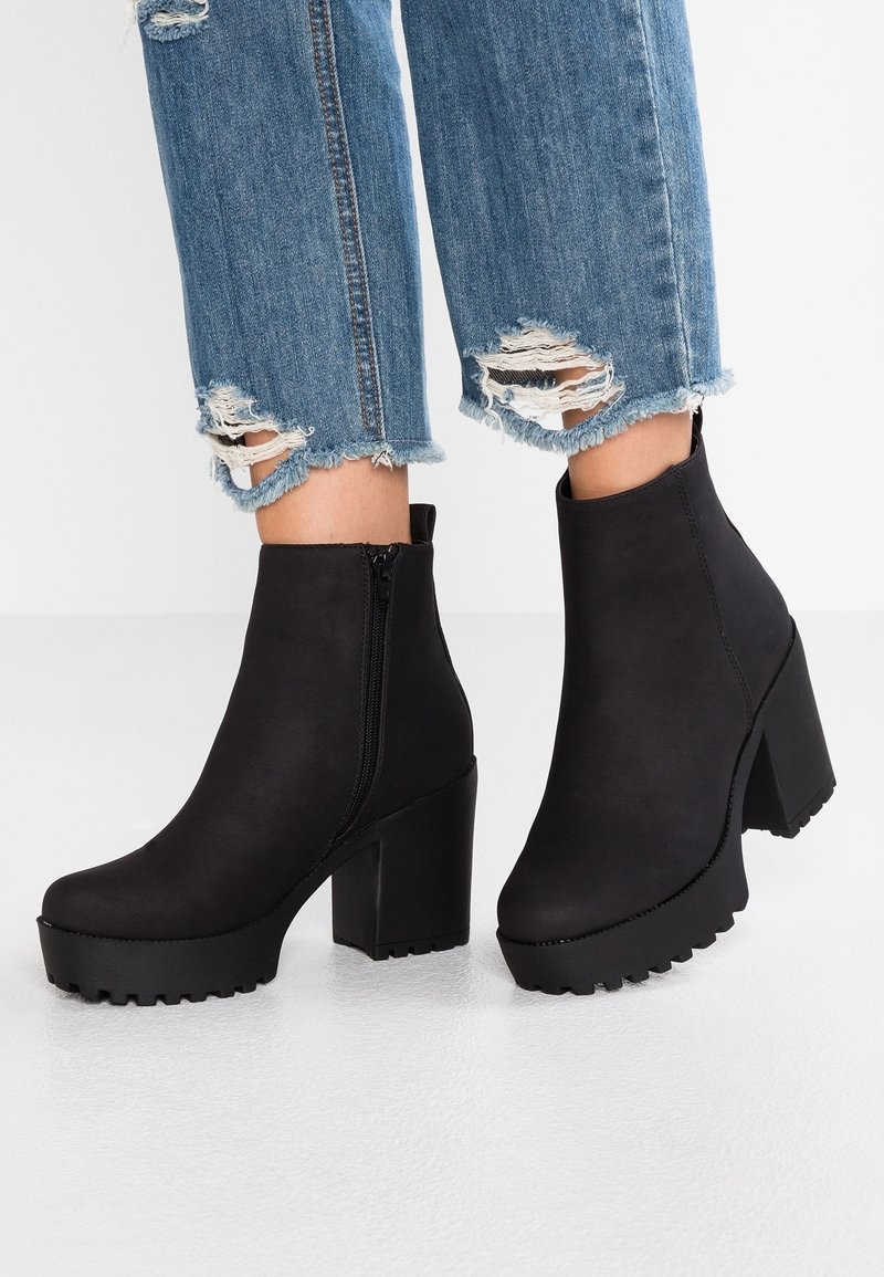 Bottines à plateforme noire avec talons épais portées avec un jean bleu déchiré et raccourci.