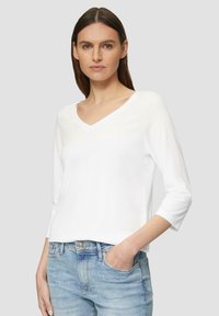 Witte lange mouwen V-hals top gemaakt van zacht katoen. Kenmerkt zich door een relaxte pasvorm en casual ontwerp, gecombineerd met lichtblauwe jeans.