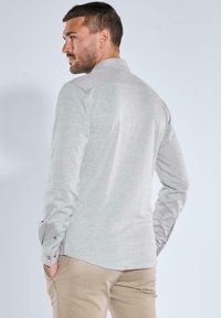 Hellgraues, strukturiertes Langarmhemd mit Kragen und knöpfbaren Manschetten, kombiniert mit beigen Hosen. Zeigt eine taillierte Passform und ein dezentes Muster.