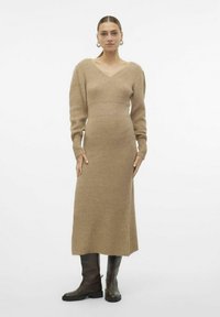 Abito lavorato a maglia, maniche lunghe, scollatura a V color beige, aderente al busto, svasato nella parte inferiore, realizzato in tessuto testurizzato, abbinato a stivali marroni fino al ginocchio.