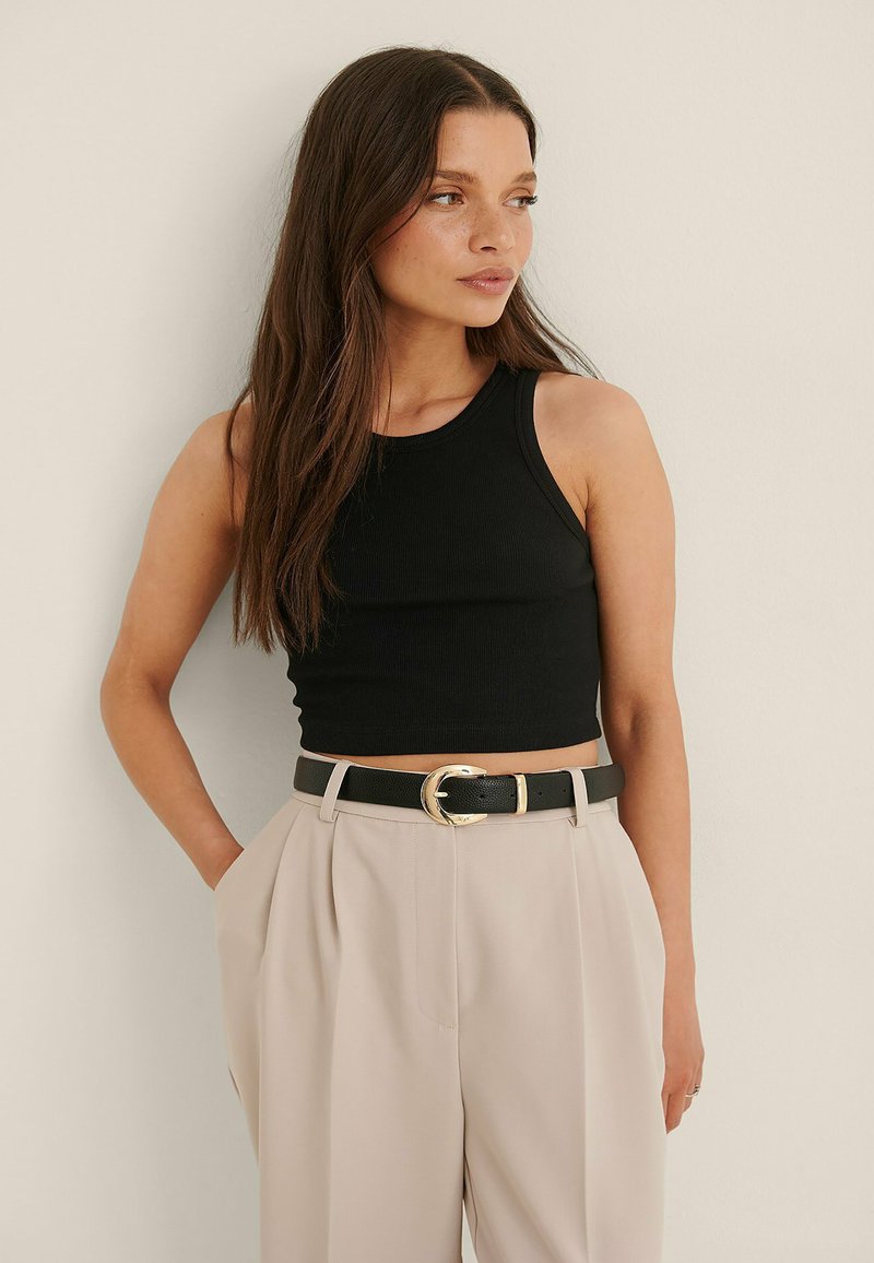 Črna žametna majica brez rokavov, v kombinaciji s kremnimi hlačami z visokim pasom. Oblačilo vsebuje tudi črn pas z zlatim sponko.