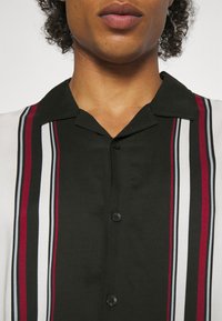 Camicia button-up con un corpo nero e righe verticali in rosso, bianco e grigio. Tessuto morbido e design colletto classico.
