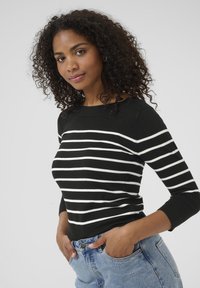 Maglione a righe bianche e nere in maglia con collo rotondo e maniche lunghe, abbinato a jeans in denim azzurro chiaro a vita alta.