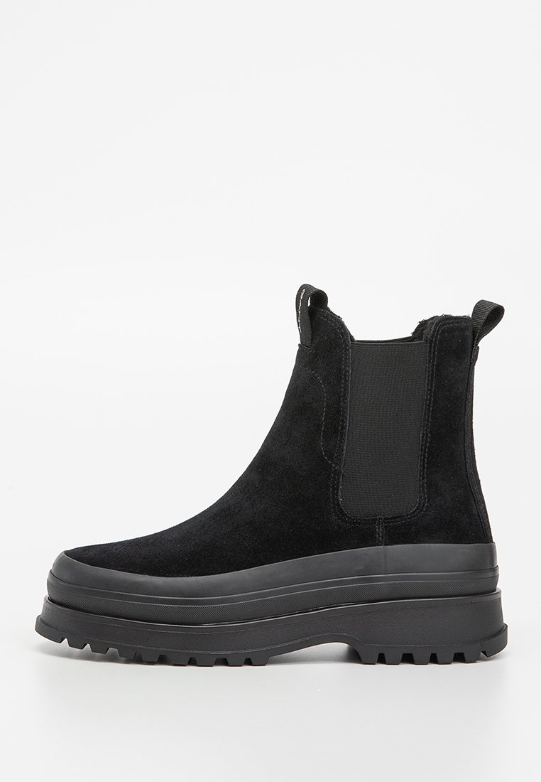 Botas Chelsea de ante negro con paneles elásticos en los laterales, punta redondeada y suela de goma gruesa con un patrón texturizado para mayor agarre.