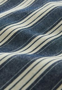 Tissu rayé bleu et blanc avec un tissage texturé créant des plis doux et ondulés.