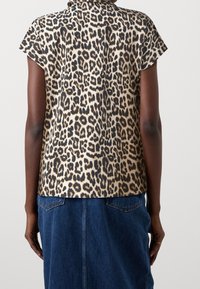 Beige und schwarze Bluse mit Leopardenmuster und kurzen Ärmeln. Verfügt über einen klassischen Kragen und eine lockere Passform, kombiniert mit einem Jeansrock.