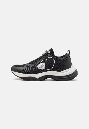 Sneaker nera con tomaia in rete, dettagli bianchi, suola texturizzata e logo a forma di cuore. Presenta lacci a contrasto e colletto imbottito.