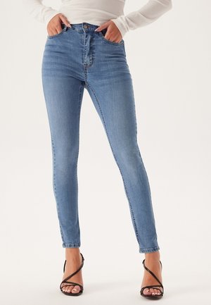 Hogebroekje in lichtblauwe denim met een skinny fit. Voorzien van voorzakken en minimale vervaging, gecombineerd met zwarte gespsandalen.
