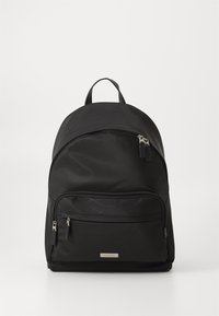 Mochila negra de nylon con parte superior redondeada, dos compartimentos con cremallera y un asa de tela. Herrajes plateados y una placa de logo en el frente.