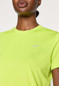 Lyhythihainen, kirkas neonkeltaisen värinen urheilupaita, joka on valmistettu sileästä kankaasta ja jossa on hillitty hopeinen Nike-logo rinnassa.