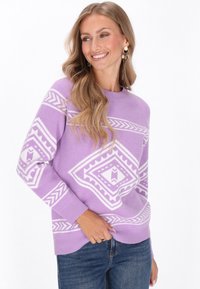 Lila trui met witte geometrische patronen, een ronde hals en geribbelde manchetten; gedragen met denim jeans. Zachte textuur, losse pasvorm.