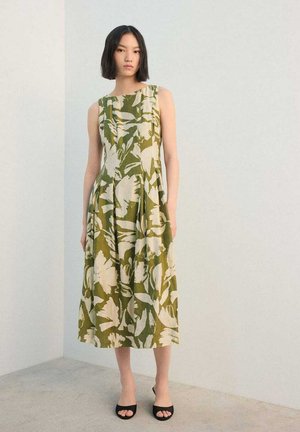 Groene jurk met bloemprint, boothals, mouwloos ontwerp en geplooide rok. Zwarte open sandalen maken de outfit compleet.