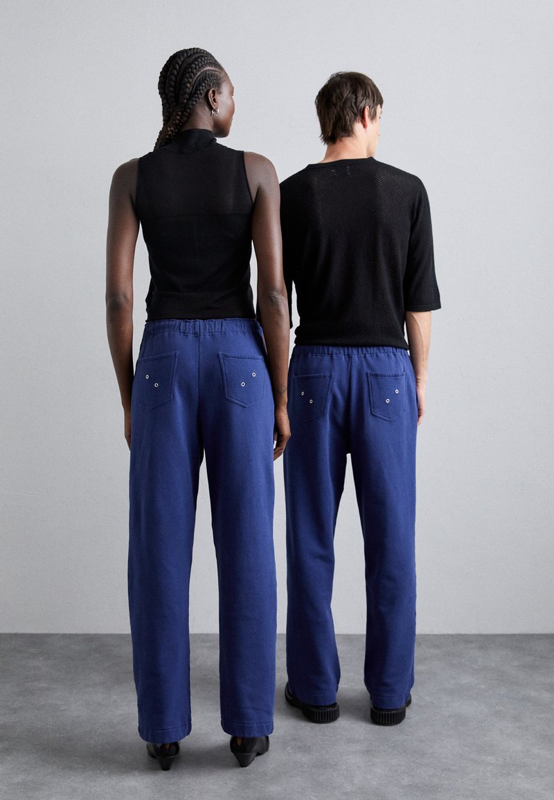 Blaue Baumwollmischungshosen mit elastischem Bund, ausgestattet mit zwei Gesäßtaschen und Metallelementen, kombiniert mit schwarzen enganliegenden Oberteilen.