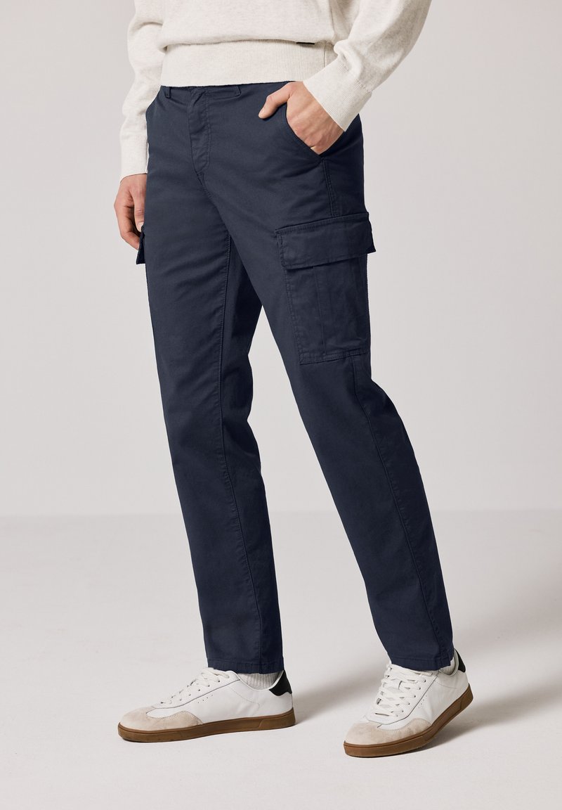 Navy cargo pants made of cotton with side pockets, straight fit, and clean design, paired with white and gray sneakers.