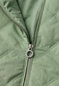 Grønt quiltet stof med en delvist åbnet sølvlynlås med en rund trækkeanordning indgraveret med "ONESTREET."