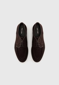 Dark brown suede shoes with a smooth finish, featuring laces, a rounded toe, and contrasting stitching along the edges. Comfortable design.