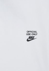 Biely bavlnený tričko s čiernym nápisom "LEN OFICIÁLNE POUŽITIE" a logom Nike, umiestnené na hrudníku v tučnom, modernom písmene.