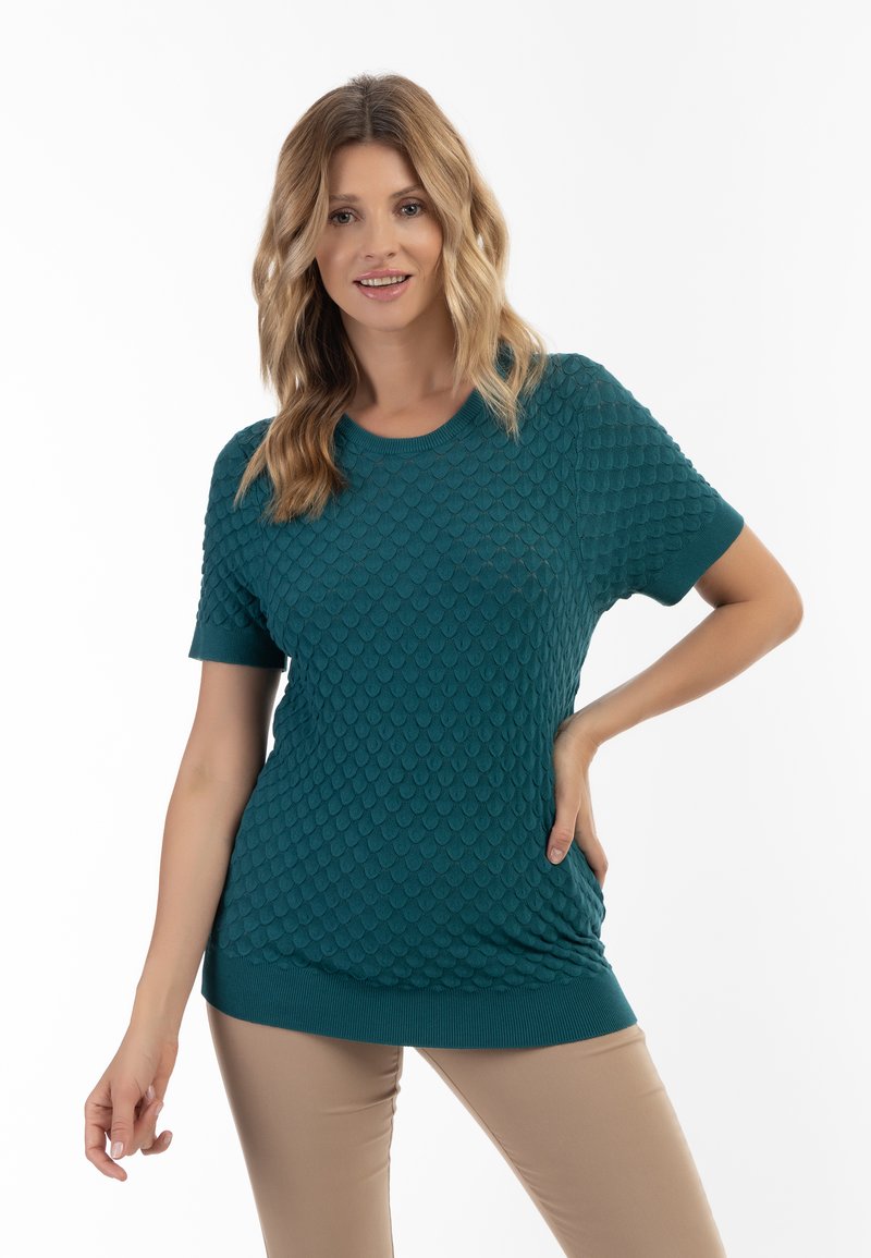 Top tricotat scurt din bumbac, de culoare teal, cu un model texturat în formă de solzi, guler rotund și tiv riblat, asortat cu pantaloni bej mulați.