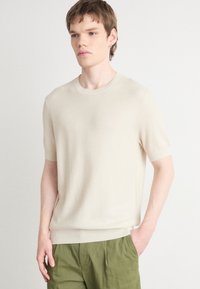 Maglione lavorato a maglia beige a maniche corte, con texture a coste, colletto rotondo e vestibilità rilassata. Abbinato a pantaloni verdi di taglio largo.