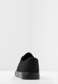 Baskets en toile noire avec un bout rond, un col rembourré et une tige texturée. La chaussure possède une semelle en caoutchouc noire plate et des détails de couture minimalistes.