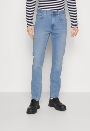 Person trägt hellblaue Slim-Fit-Jeans, schwarze klobige Schnürschuhe, weiße Socken und ein schwarz-weiß gestreiftes Langarmoberteil.