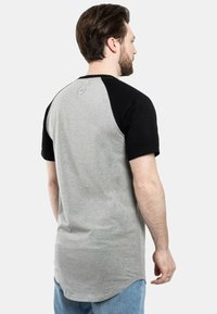 Harmaa ja musta raglan-paita lyhyillä hihoilla, kaarevalla helma ja huomaamaton logo takana. Valmistettu pehmeästä, hengittävästä kankaasta.