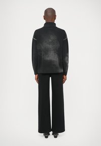Suéter preto com gola alta, apresentando um gradiente texturizado e costuras desportivas. Combinado com calças pretas de perna larga e sapatos de salto.