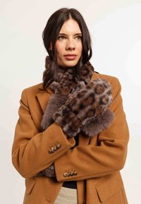 Faux kažokādas leopardu raksta šalle un cimdi brūnos un bēšos toņos, valkāti virs pelēka mēteļa ar zelta pogu akcentiem. Mīksta tekstūra.