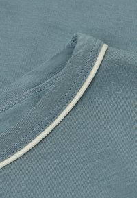 Blå randig tyg med en ljus crèmefärgad krage. Texturen är slät och något elastisk, lämplig för avslappnad användning.