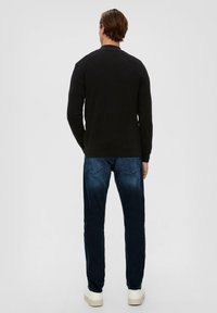 Schwarzer, gerippter Pullover mit langen Ärmeln, schmaler Schnitt, Rundhalsausschnitt und Raglanärmeln, kombiniert mit dunkelblauen Jeans und beigen Sneakers.