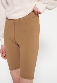 Shorts da bici marroni, elasticizzati, con una texture liscia, caratterizzati da un orlo cucito e un piccolo numero ricamato "10" sulla vita.
