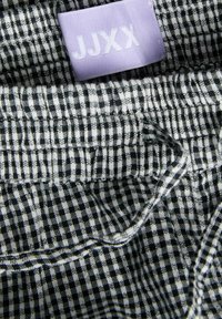 Κοντινό πλάνο υφάσματος σε ασπρόμαυρο καρό με ετικέτα ρούχου λεβάντας που γράφει "JJXX" ραμμένη στο εσωτερικό του ρούχου.