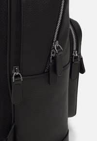 Μαύρο δερμάτινο σακίδιο πλάτης με υφή, πολλαπλούς φερμουάρ και λείες μεταλλικές λεπτομέρειες. Πλευρικές τσέπες για επιπλέον αποθηκευτικό χώρο.