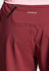 Bordowe spodenki sportowe z teksturowanej tkaniny, z małą kieszonką na zamek błyskawiczny oraz logo "AEROREADY" na tylnym pasie.