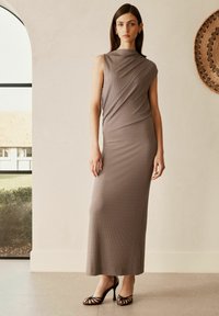 Maxime dress in beige ribbi-kangas, joka sisältää epäsymmetrisen pääntien, tiukan siluetin ja sivuhalkion. Yhdistetty mustiin nauhakorkokenkiin.