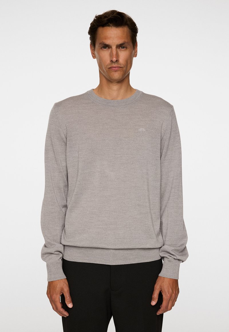 Vaaleanharmaa neulepaita, jossa on pitkät hihat ja pyöreä kaula-aukko. Paita on varustettu ribbi-harteilla ja hihansuilla. Rintakehässä on hienovarainen logotavoite.