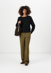 Maglione nero a maglia, pantaloni a gamba larga oliva, borsa in suede marrone con zip argentata, mocassini marroni con dettagli in hardware dorato.