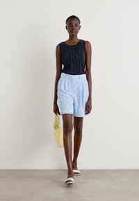 Black sleeveless top with vertical pleats, light blue shorts with white polka dots, white sandals, and a yellow handbag. Simple, casual outfit.