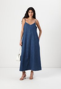 Denim maxikjole med tynne stropper, V-hals og frontknappedetaljer. Har sidelommer og faller til ankellengde.