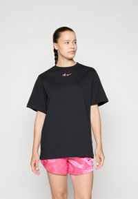 Black cotton t-shirt with a crew neckline and short sleeves; features a pink Nike logo on the chest. Paired with shiny pink shorts.