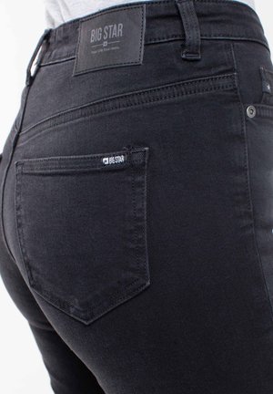 Melnas džinsu bikses ar augstu jostasvietu, ar izšūtu plāksnīti aizmugurējā jostasvietā un mazu zīmolu etiķeti aizmugurējā kabatā.