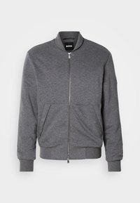 Giacca bomber grigia realizzata in tessuto morbido, con chiusura a zip frontale, polsini a costine e due tasche frontali. Design semplice con branding minimale.