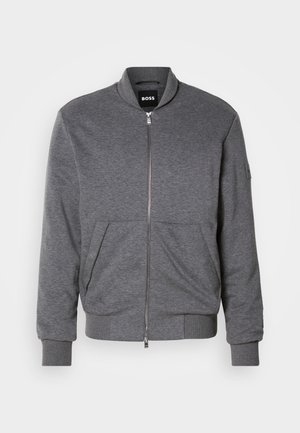 Giacca bomber grigia realizzata in tessuto morbido, con chiusura a zip frontale, polsini a costine e due tasche frontali. Design semplice con branding minimale.