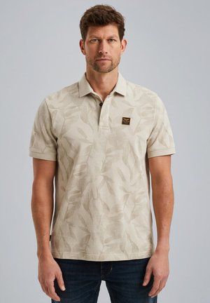 Tans polo shirt met een bladerenpatroon, korte mouwen en een kraag met drie knopen. Bevat een klein zwart en gouden merklogo op de borst.