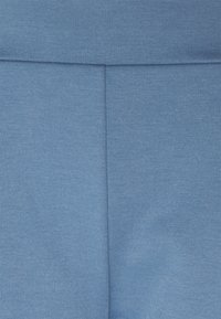 Světle modrá elastická tkanina s hladkým povrchem, se švem uprostřed. Navržena pro pohodlí a flexibilitu.