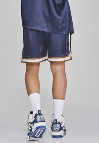Marineblaue Sportshorts mit einem strukturierten Muster, goldenen Akzenten am Saum, kombiniert mit weißen Socken und blau-weißen Turnschuhen.