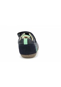 Zapato azul marino con textura de ante, correa ajustable y acento verde en el talón; suela de goma para mayor agarre, con forma redondeada.