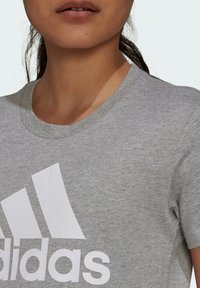 Szara bawełniana koszulka z okrągłym dekoltem i krótkim rękawem. Z przodu znajduje się duże, białe logo Adidas. Miękka faktura.